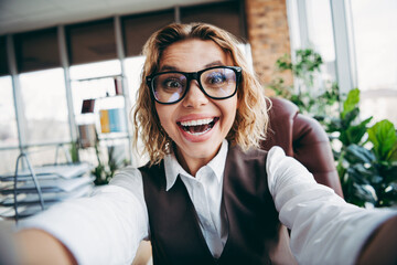 Smiling female professional in stylish formalwear taking selfie in office with plants and natural...