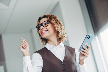 Confident businesswoman holding smartphone in modern office, exhibiting success and professionalism