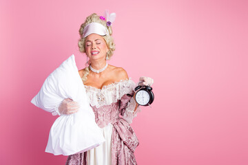 Elegant woman dressed in historical attire holding a clock and pillow against a pink backdrop