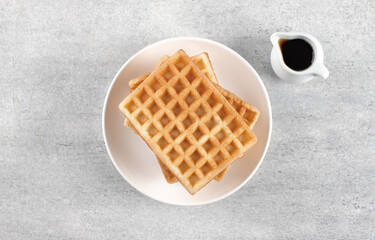 Stack of golden belgian waffles with maple syrup on grey background. Top view. Breakfast or dessert concept.