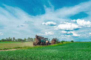 Naklejka premium Liquid manure spreader, tractor with tank spraying liquid manure into the soil on field. Agricultural landscape.