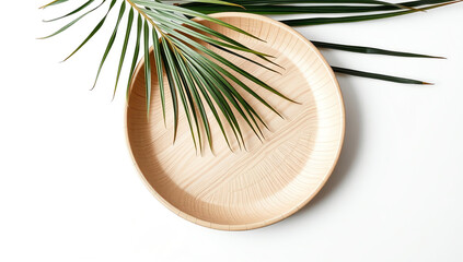 Minimalist flat lay of an empty round wooden plate with a tropical palm leaf on a white background. Eco-friendly dining concept.