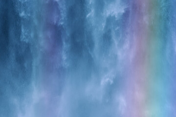 Obraz premium Water cascades down a rocky cliff, creating a vibrant mist that catches the sunlight and forms a rainbow