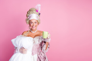 Elegant lady dressed in baroque-style costume holding a pillow and coffee, standing in front of...