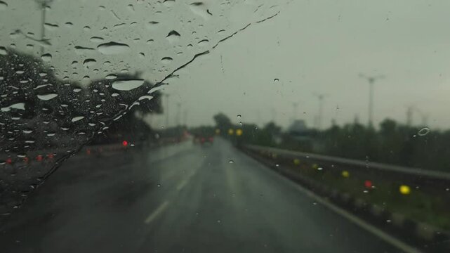 Rain-streaked window on a rainy evening, the blurred lights of the evening city, passing cars, and traffic reflected on wet glass, while windshield wipers swept across a car window.