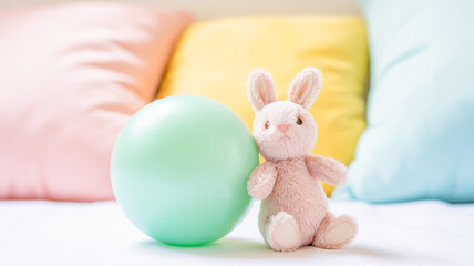 A soft, pastel photograph of a mint green spherical ball and a small plush bunny toy against a blurred background of pastel-colored cushions