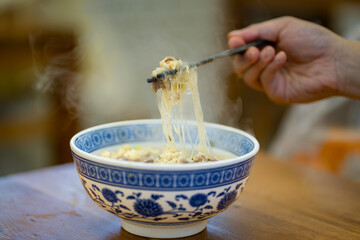 Crop anonymous male with chopsticks eating yummy mutton soup with noodles and powder in  bowl at...