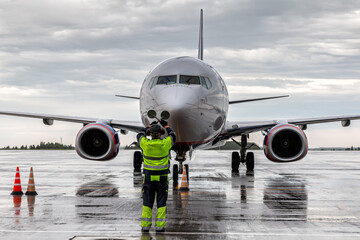 Airplane marshalling at the aiport apron in rainy weather. Passenger plane meeting