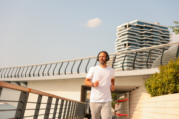 Man jogging along modern waterfront promenade under bright sun, enjoying music and fitness in urban environment