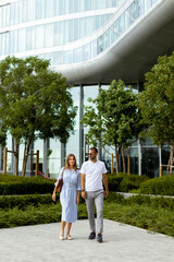 Couple strolls through lush green landscape near modern architecture on a sunny day