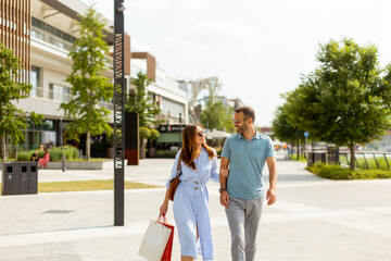 Couple enjoying a sunny day strolling through a vibrant shopping district with colorful storefronts and lush greenery