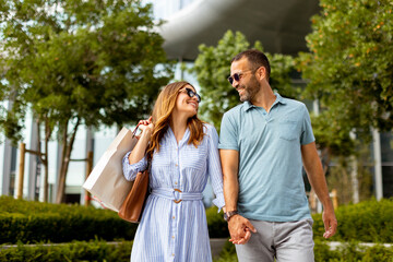 Couple strolls hand in hand through a vibrant outdoor shopping district on a sunny afternoon