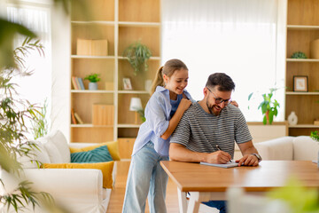 Joyful moments shared between a father and daughter while writing at home in a bright, cozy living room filled with greenery