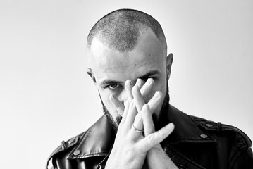 A black and white portrait of a man with hands clasped, looking directly at the camera.