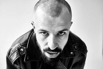A striking black and white portrait features a bald man with an intense gaze and a rugged beard.