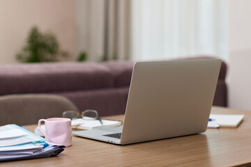 Open laptop and cup of coffee on wooden desk in a kitchen room at home office