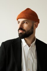 A handsome man with a beard in a stylish outfit, looking thoughtful.