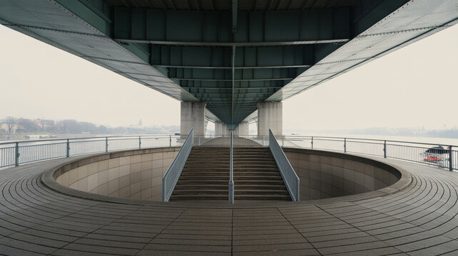 View of a circular staircase under a bridge with a river in the background on a foggy day in an urban setting