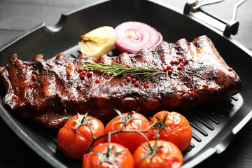 Delicious roasted pork ribs with rosemary, tomatoes and onions on grey wooden table, closeup