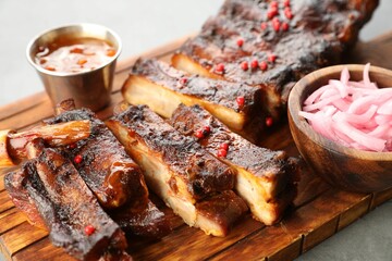 Delicious spare ribs, sauce and onion on grey table, closeup