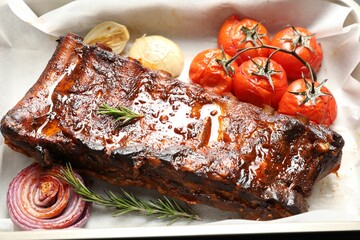 Delicious spare ribs, rosemary, baked onion and sun dried tomatoes on parchment paper, closeup