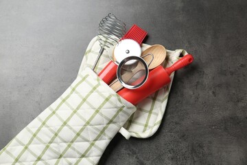 Different kitchen utensils in oven mitten on grey table, top view