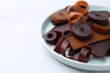 Tasty fruit leather rolls on white table, closeup. Space for text