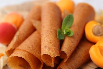 Delicious fruit leather rolls and apricots on table, closeup