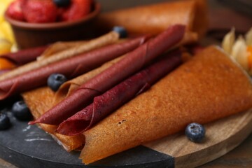 Delicious fruit leather rolls and berries on table, closeup