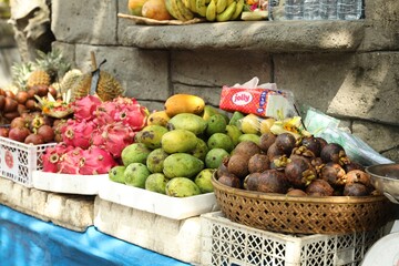 Bali, Indonesia - May 15, 2025: Fresh ripe fruits near stone building at market