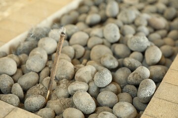 Burning incense stick in rocks indoors, closeup