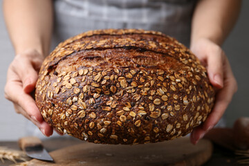 Woman with freshly baked bread at table against grey background, closeup