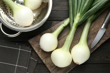 Fresh ripe green onions with cutting board and knife on black wooden table, flat lay
