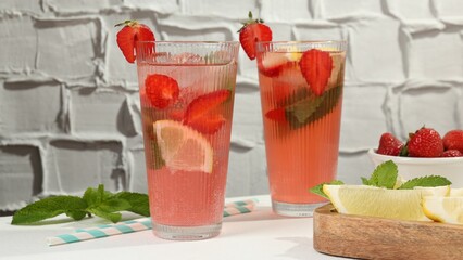 Refreshing drink with strawberries, mint, lemon and ice on white table against grey textured background, closeup
