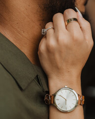Close-up of woman’s manicured hand with diamond engagement ring, gold band and leather watch resting on partner’s shoulder