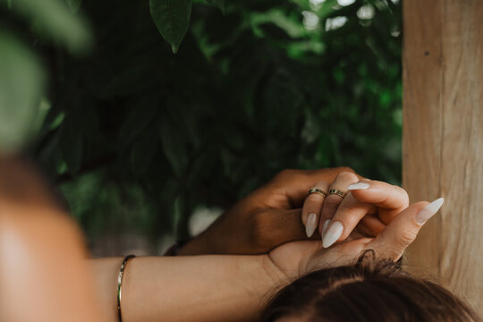 Close-up of couple holding hands showcasing gold rings and manicured nails against a leafy garden backdrop - Powered by Adobe
