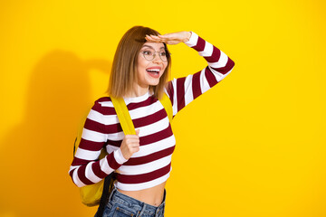 Cheerful young woman in striped top looking forward against bright yellow background with a joyful...