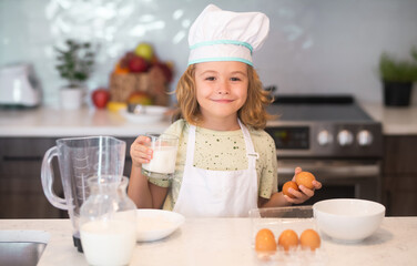 Funny kid with eggs at kitchen. Chef kid boy baking on the kitchen. Child chef cook prepares food...