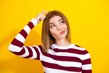 Confused young woman in striped sweater contemplating while scratching her head against vibrant...