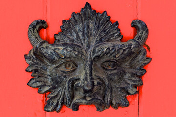 Tarnished old Brass devils mask on door is used to ward off evil spirits or negativity.