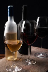 Crystal glasses with red and white wine and wine bottles,
over rustic wooden table on black background.