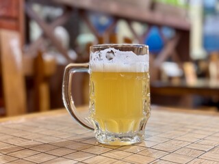 Enjoying Chilled Beer in a Charming Rustic Setting Surrounded by Bubbles and Friends. A refreshing glass of beer topped with foam sits on a rustic wooden table, creating a cozy atmosphere