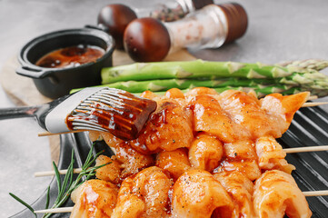 Brush with marinade sauce for marinating kebabs. Raw chicken breast kebab. Raw sliced chicken breast on wooden sticks with asparagus