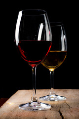 Crystal glasses with red and white wine
over rustic wooden table on black background