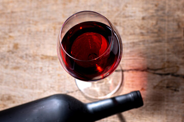 Crystal goblet with red wine and bottle on the rustic wooden table on black background