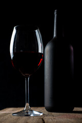 Crystal goblet with red wine and bottle on the rustic wooden table on black background
