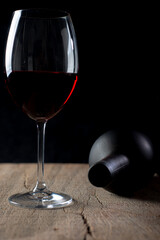 Crystal goblet with red wine and bottle on the rustic wooden table on black background