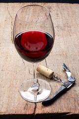 
Crystal goblet with red wine and corkscrew on the rustic wooden table and on black background.
