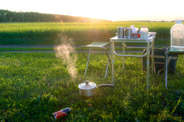 Stainless steel pot on a burner with steam in the evening light outdoors. Picnic by the road during a trip.