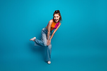 Cheerful young woman posing on blue background wearing casual colorful top and jeans, expressing...